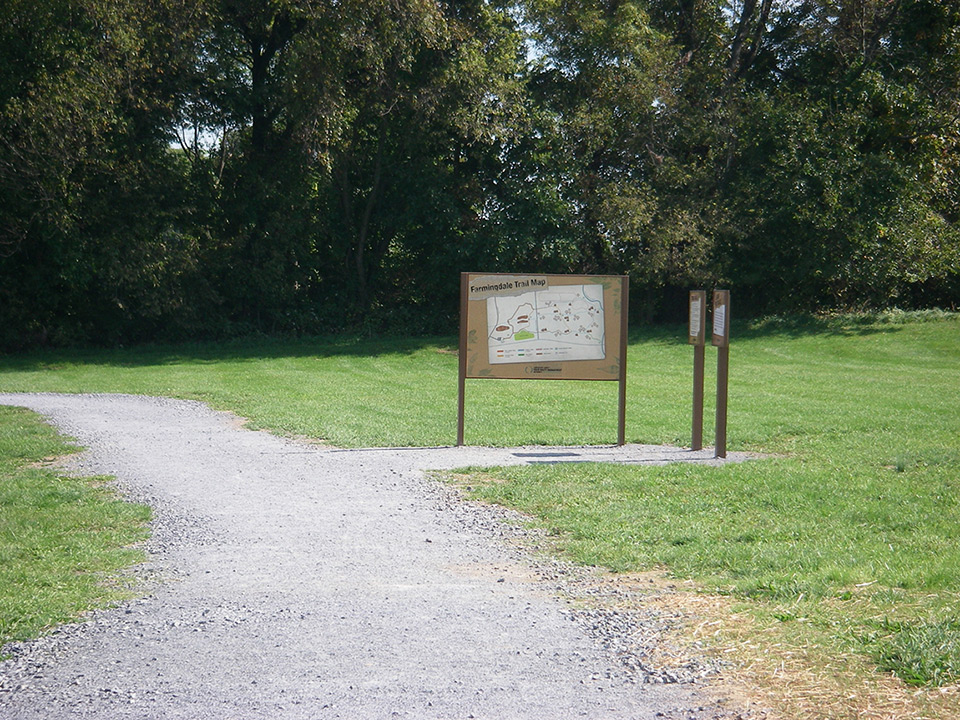 A photo of a trail with a wooden sign that says "Farmingdale Trail"