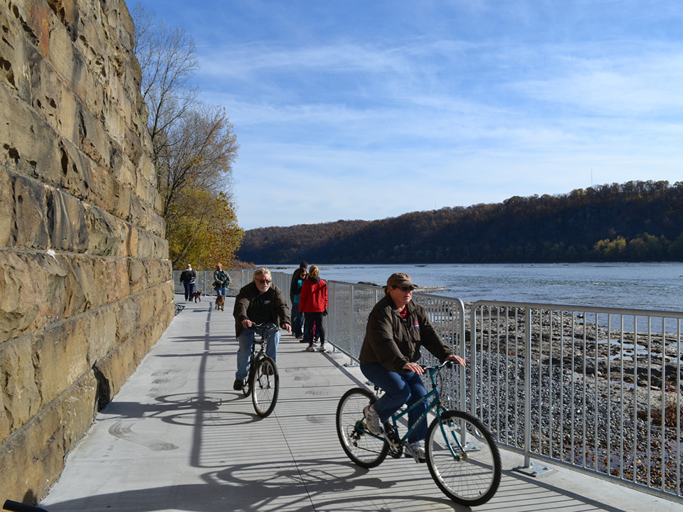 People riding their bikes and walking along a trail beside a river